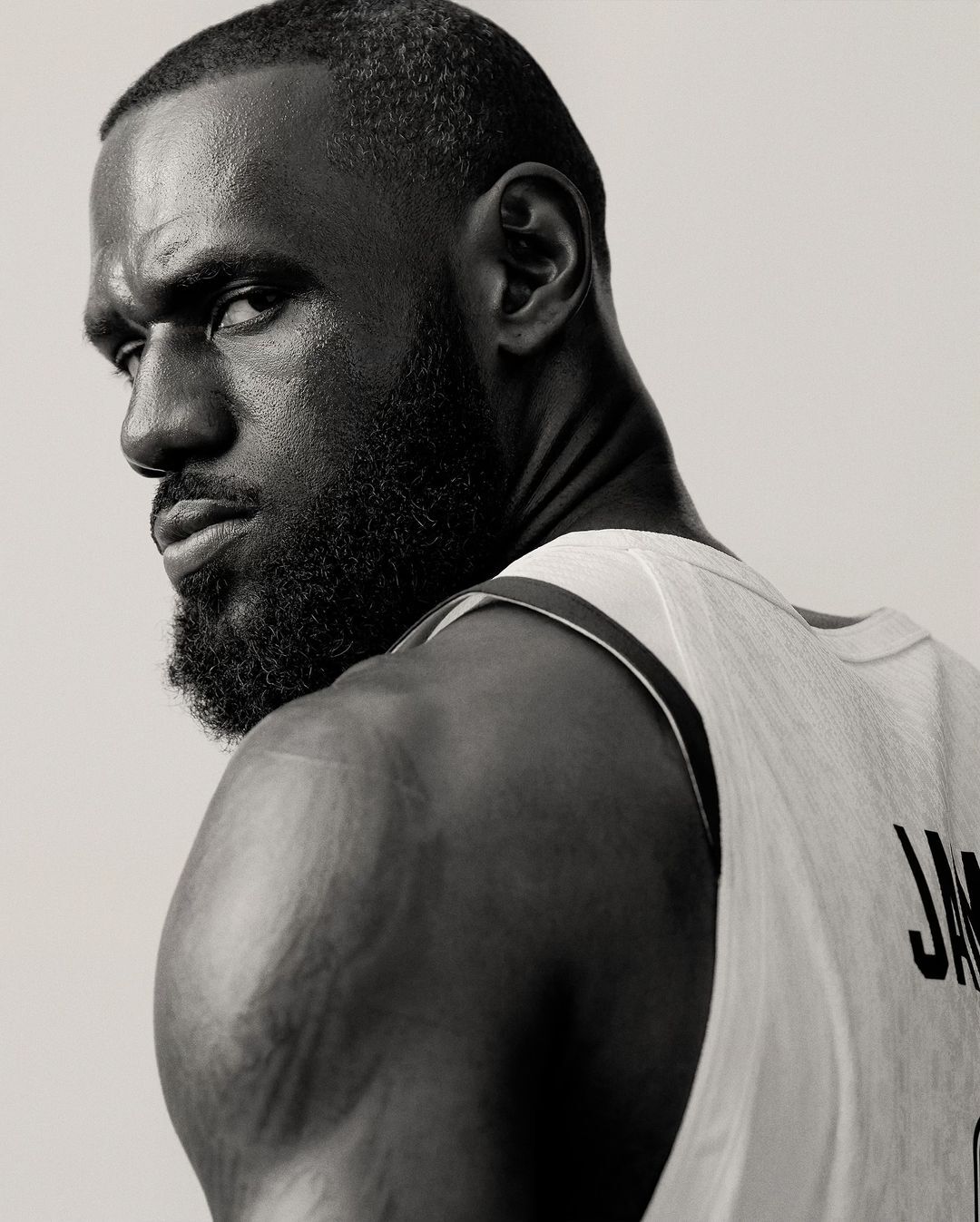 Monochrome portrait of LeBron James in athletic wear, looking over his shoulder with a serious expression against a neutral background.