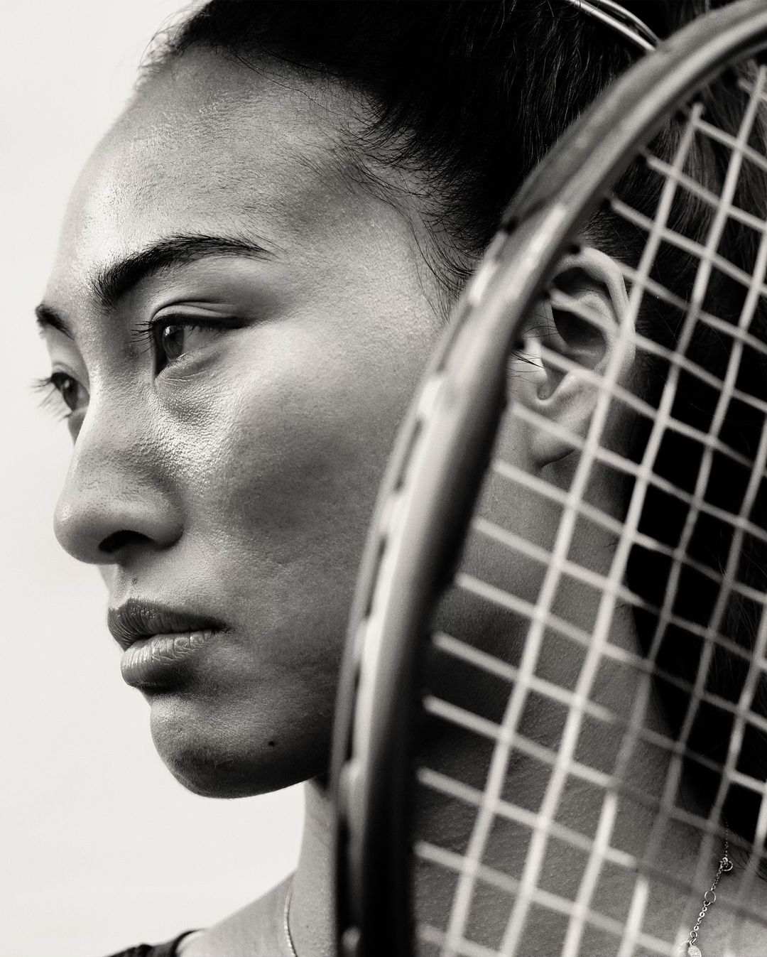 Profile portrait of an Asian adult female tennis player posing with a racket, in black and white with a neutral facial expression.