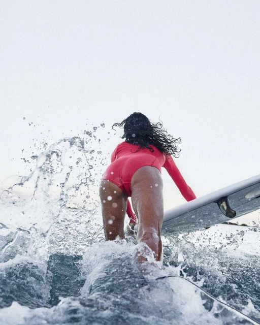 Woman in a pink wetsuit is surfing on a wave with a surfboard. The shot is from behind with the focus on the surfer.