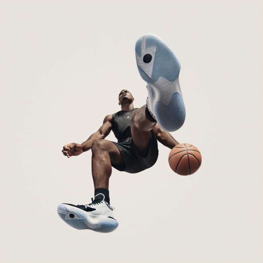 Athlete in black activewear leaps with a basketball, highlighting black, white, and light blue athletic shoes against a white background.