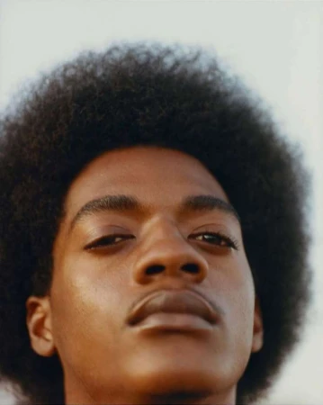 Close-up portrait of a young Black man with a voluminous afro hairstyle captured from a low angle.