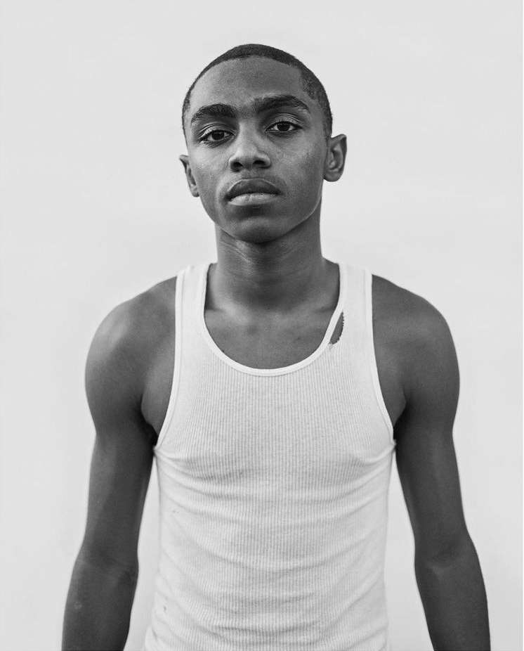 Portrait of a young Black man wearing a white ribbed tank top against a plain light background