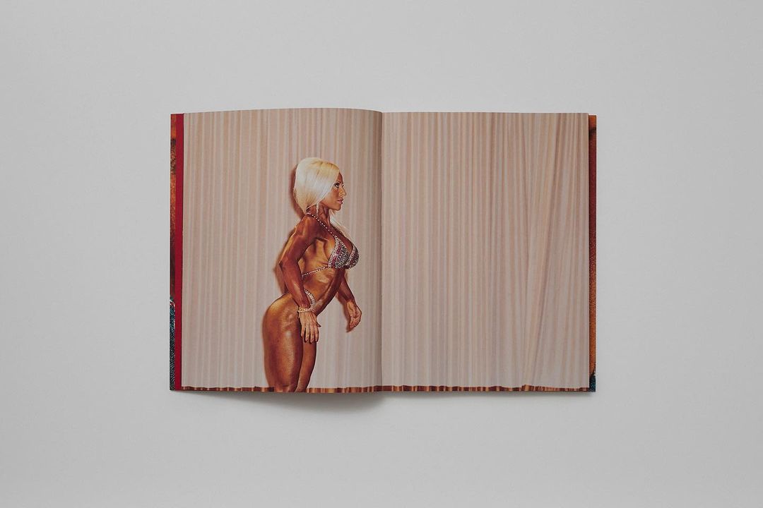 A woman with blond hair poses in a glittering bikini on stage with a neutral backdrop, displayed as a photograph in an open book.