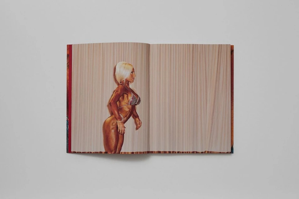 A woman with blond hair poses in a glittering bikini on stage with a neutral backdrop, displayed as a photograph in an open book.