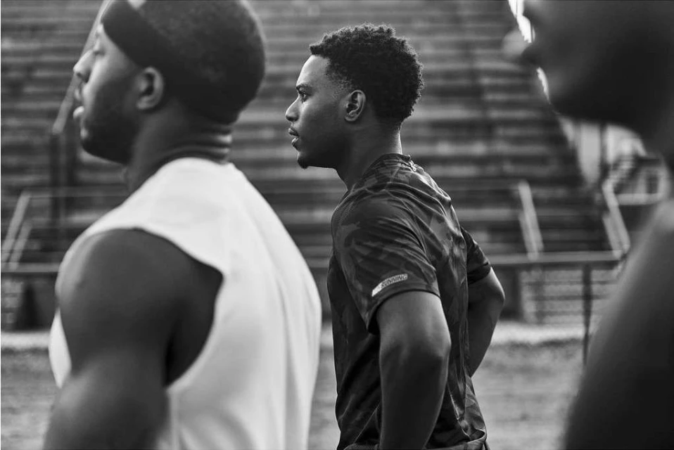 Monochrome shot of three African American men in athletic wear standing outside, facing right, in a close up, eye-level, outdoor composition.