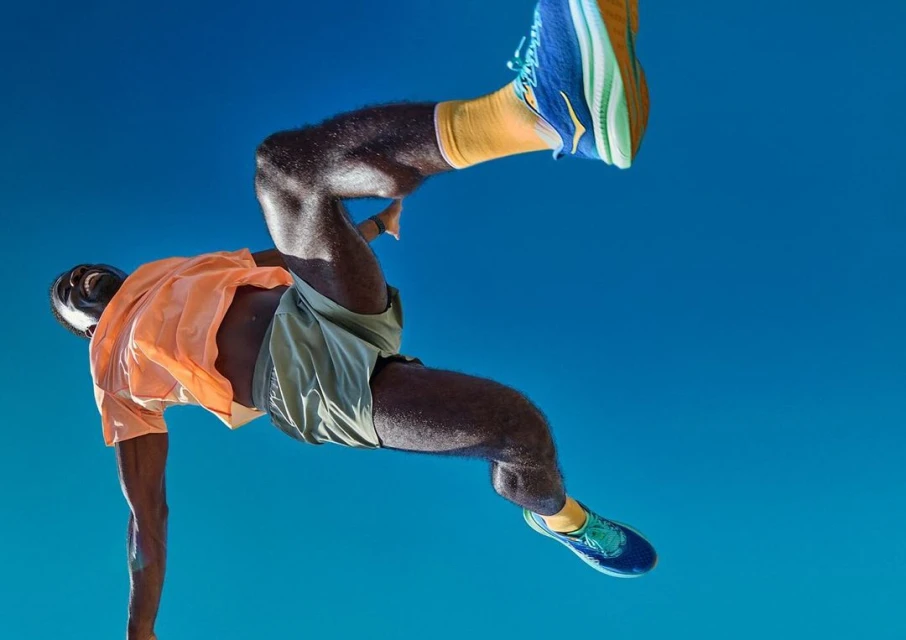 Action shot of a Black male athlete in mid-air wearing sportswear against a clear blue sky, emphasizing movement and athletic apparel.