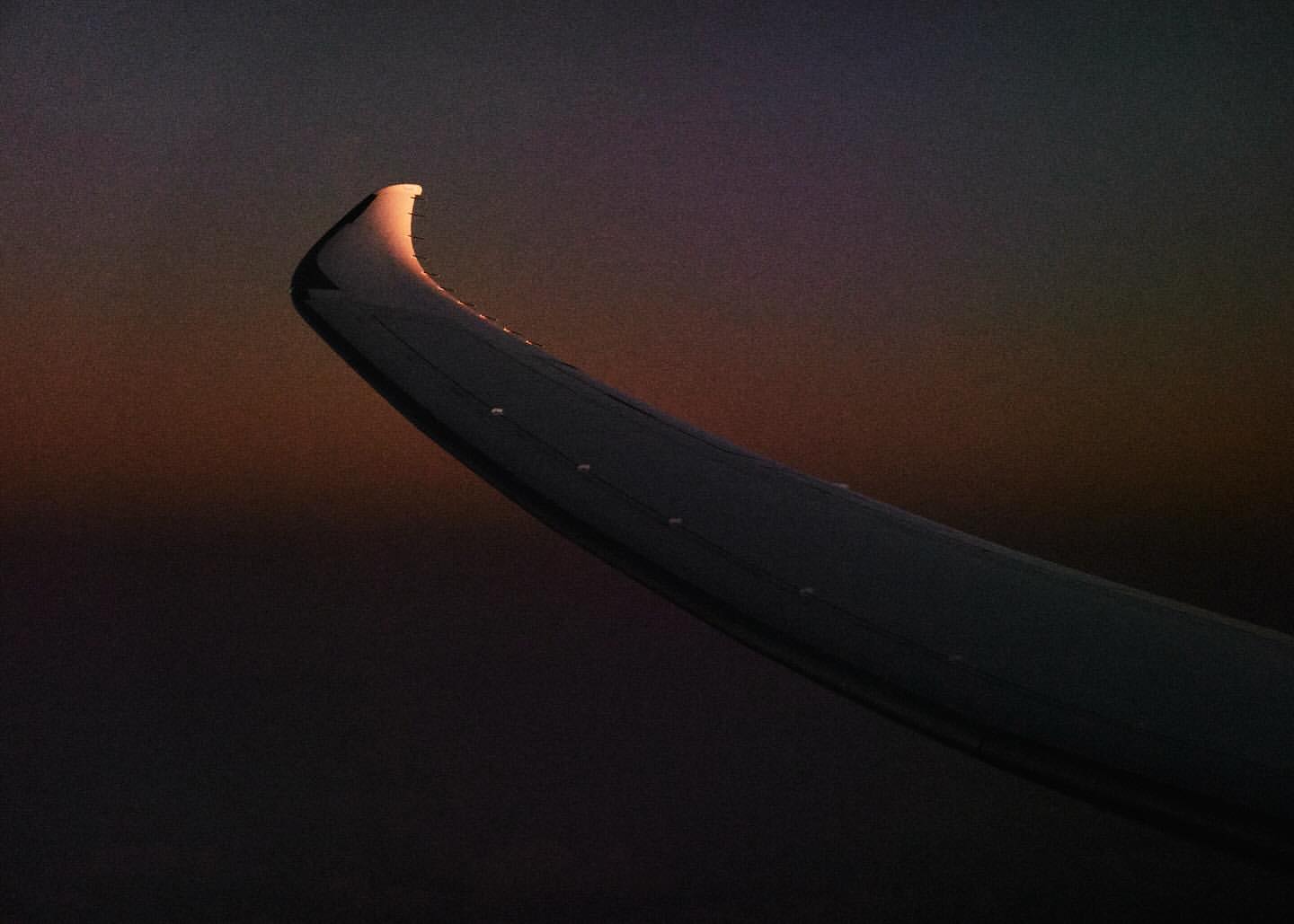 Airplane wing in flight against a vibrant sky with colors of orange, purple, and grey visible through the window during golden hour.