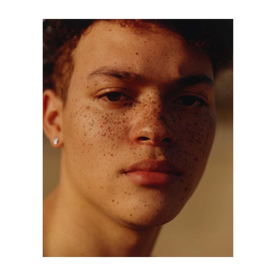 Close-up portrait of a young man with freckles and dark curly hair by photographer Anthony Blasko