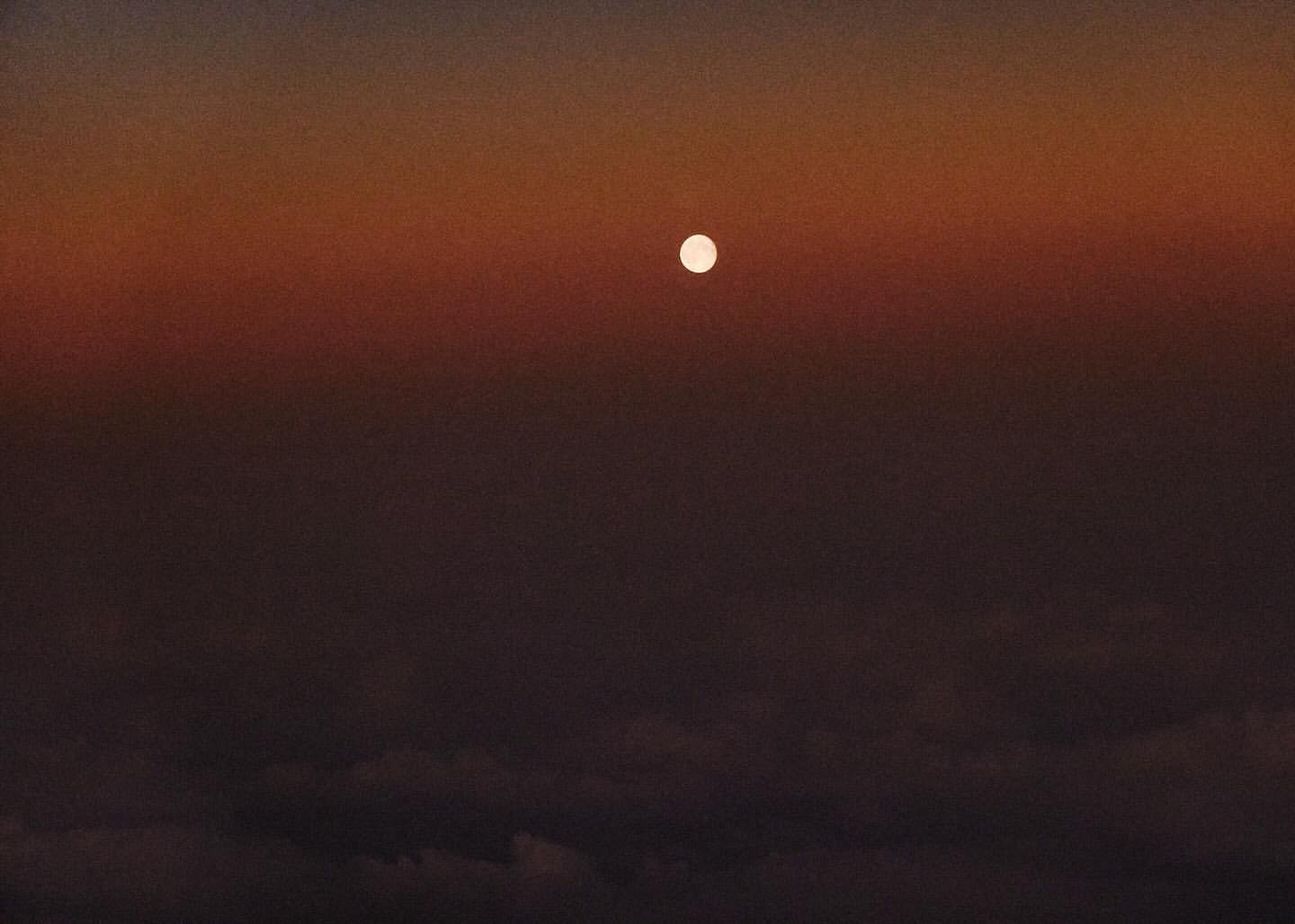 Dramatic sky with the sun visible above clouds, creating a vivid color gradient from dark brown to vibrant orange.