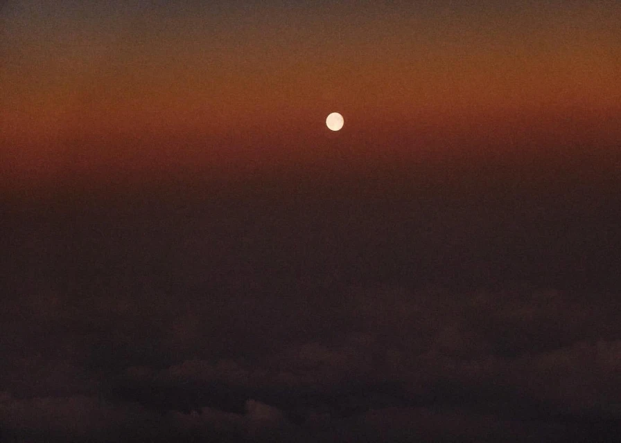 Dramatic sky with the sun visible above clouds, creating a vivid color gradient from dark brown to vibrant orange.