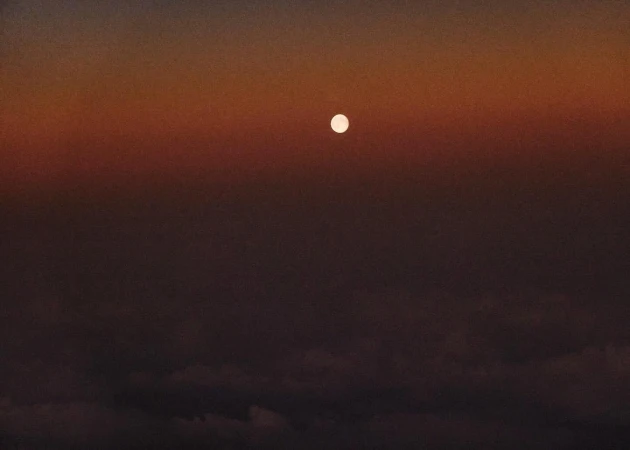Dramatic sky with the sun visible above clouds, creating a vivid color gradient from dark brown to vibrant orange.