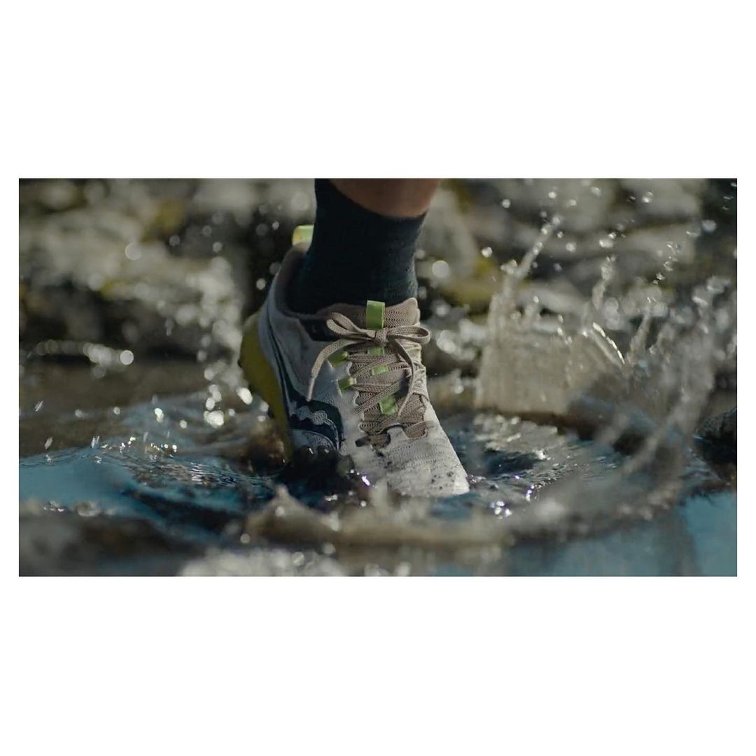 Close-up of a Saucony running shoe splashing through a puddle, showcasing its design and water resistance during outdoor activity.