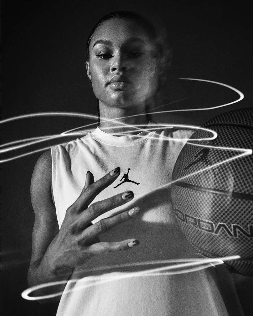 Black and white portrait of a woman in a Jordan tank top holding a basketball with light painting effects against a dark background.