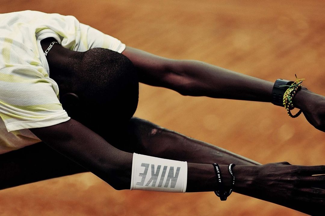 Athlete stretching with arms outstretched wearing Nike branded wristbands on a clay surface in bright light. Sports and activewear concept.