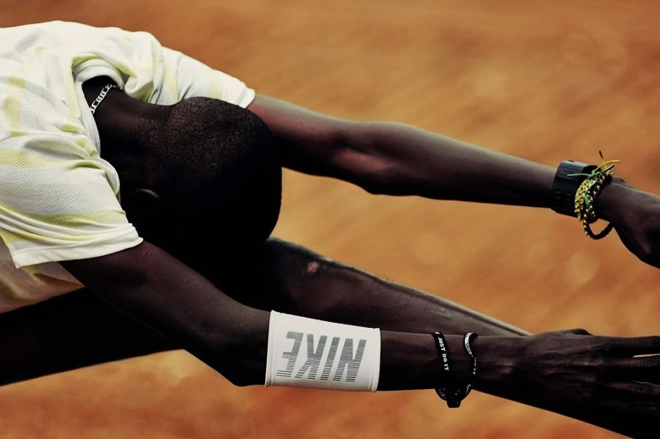 Athlete stretching with arms outstretched wearing Nike branded wristbands on a clay surface in bright light. Sports and activewear concept.
