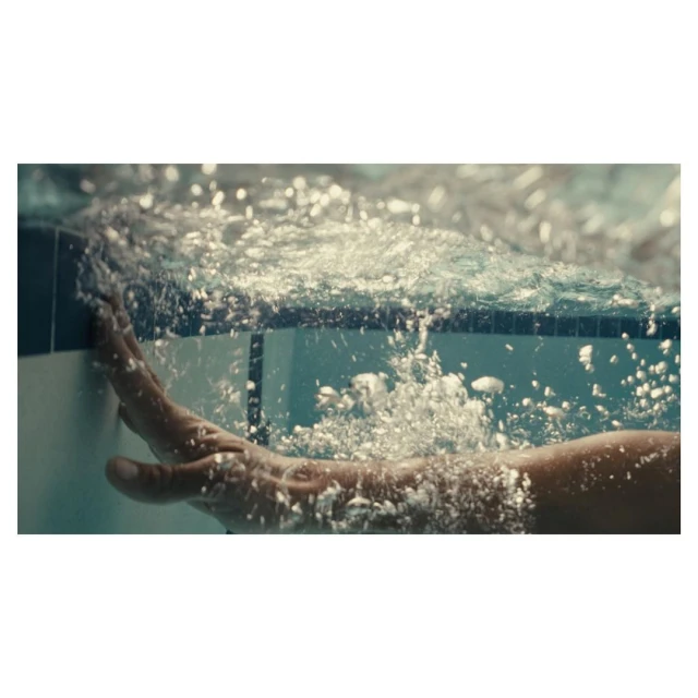 Underwater view of a person's arm and hand touching the edge of a swimming pool, with bubbles and filtered light creating a tranquil scene.