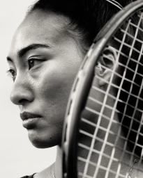 Close-up black and white portrait of a female athlete framed behind a tennis racket strings by Anthony Blasko.