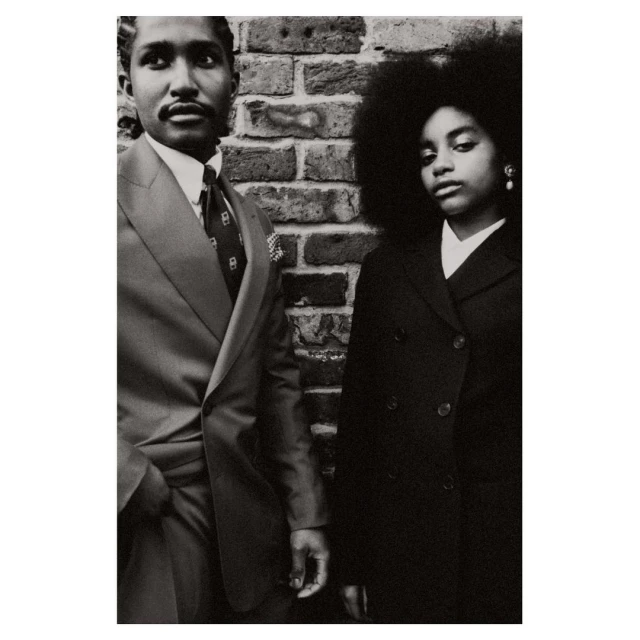 Black and white portrait of an African American couple in suits standing against a brick wall, exuding vintage fashion and style.