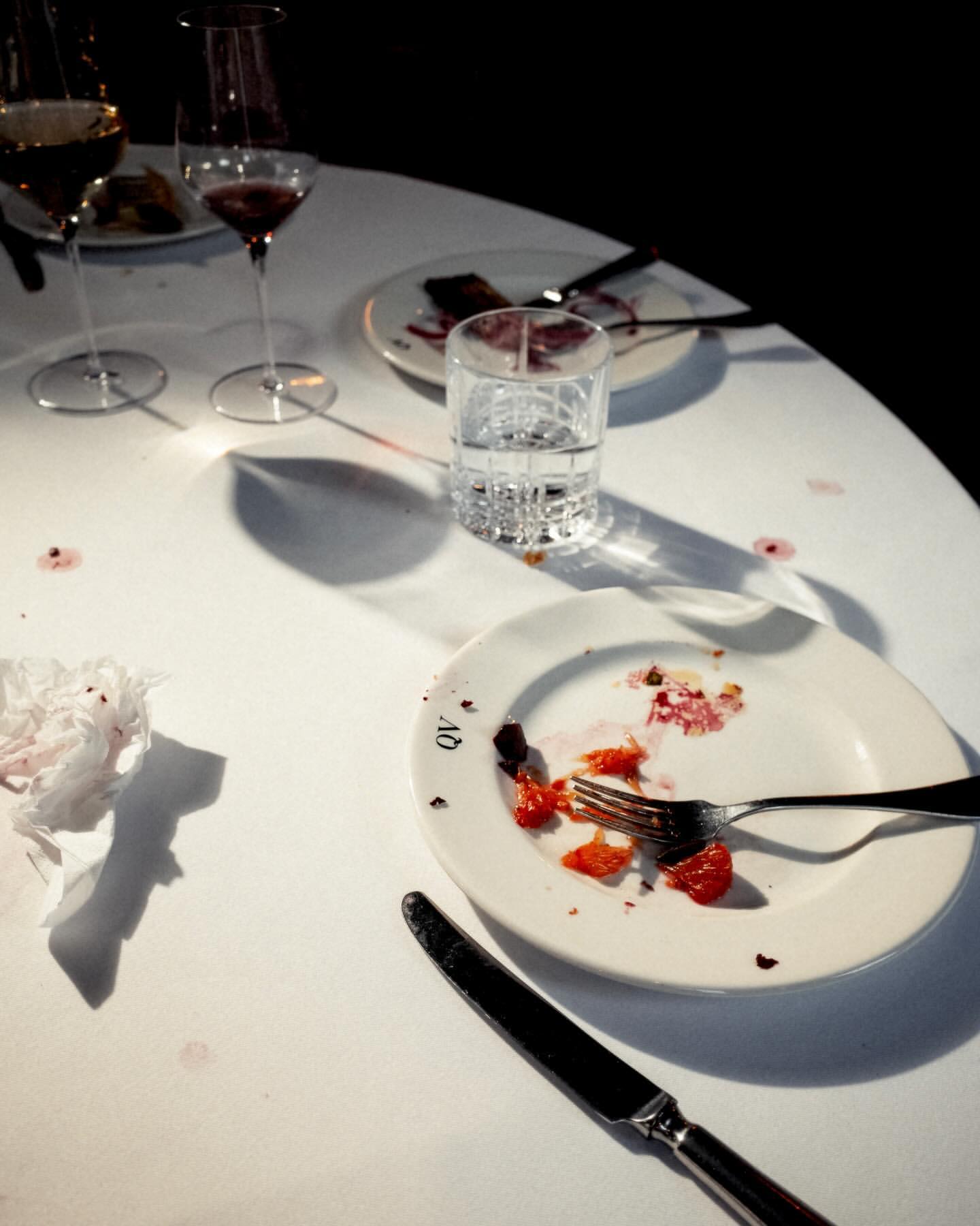 Empty plates, silverware, and glasses on a white round table after a meal in a restaurant, showing leftovers, crumbs, and stains.
