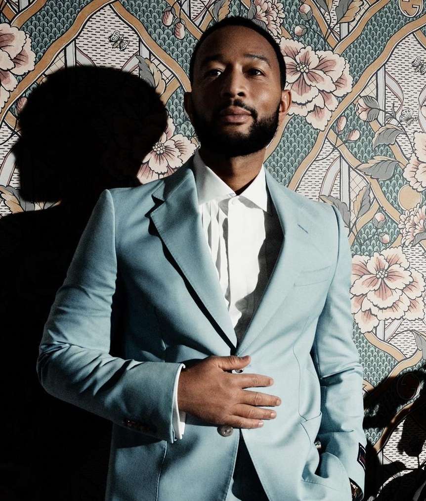 Portrait of a handsome adult man in a light blue suit, posing against a floral wallpaper in a photo studio with dramatic lighting.