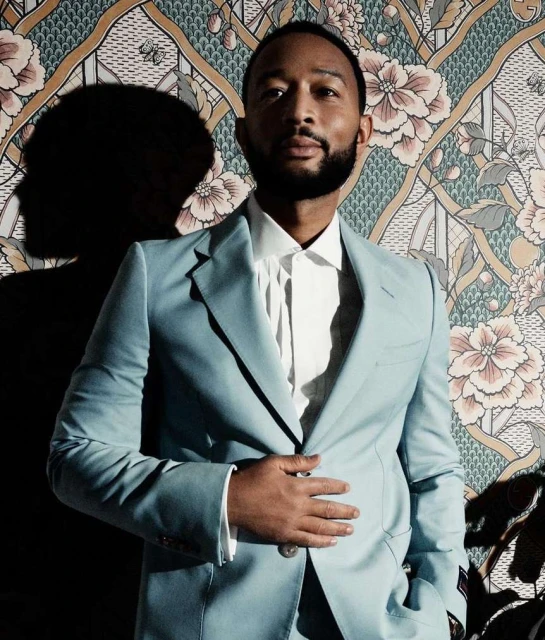 Portrait of a handsome adult man in a light blue suit, posing against a floral wallpaper in a photo studio with dramatic lighting.