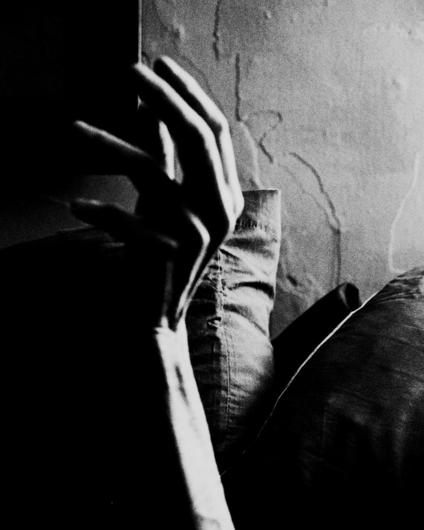Close-up shot of a hand and forearm, creating a study in light and shadow, along with textured wall and shirt details.