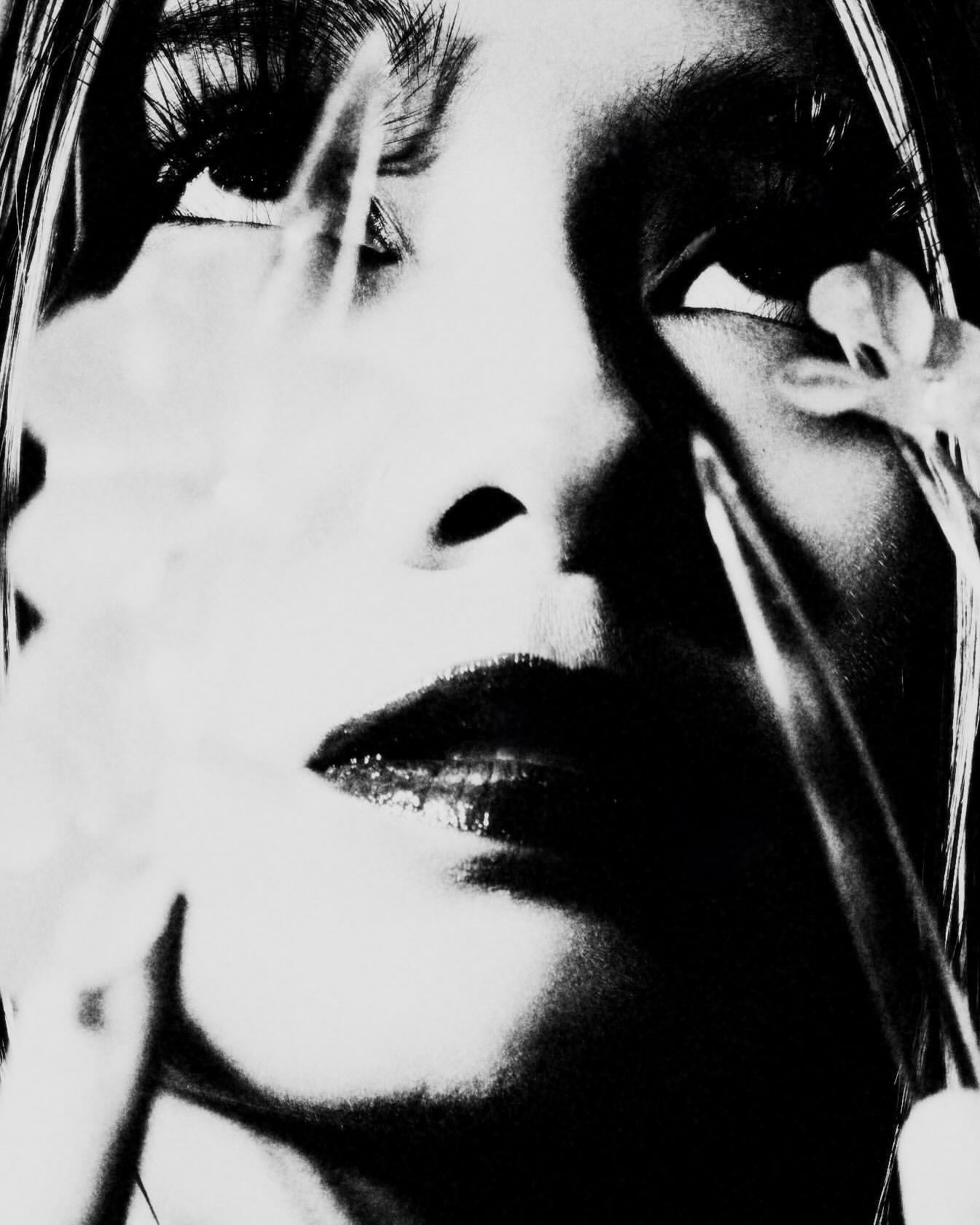 Monochromatic portrait of a woman's face partially obscured by white flowers, emphasizing dark tones and close-up perspective.
