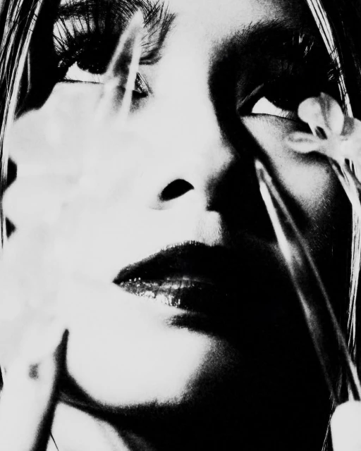 Monochromatic portrait of a woman's face partially obscured by white flowers, emphasizing dark tones and close-up perspective.