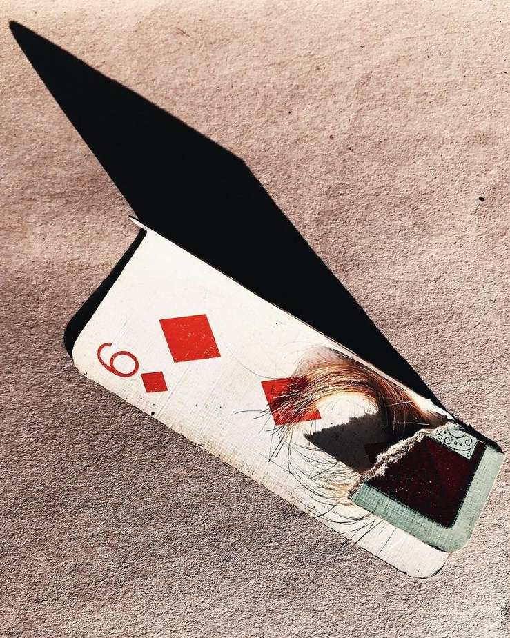 Close-up still life: A damaged playing card, the nine of diamonds, is visible against a textured background with a prominent shadow.