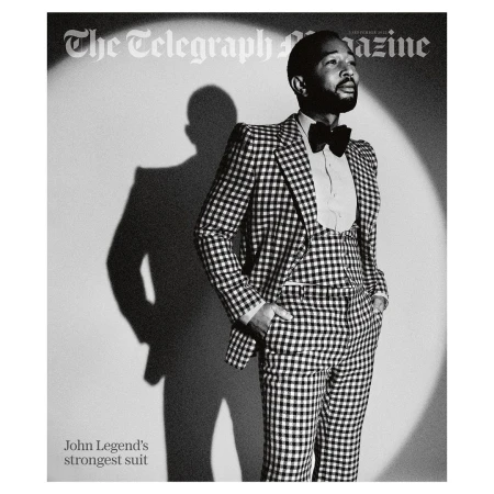 John Legend in a black and white magazine cover photo. He is wearing a checkered suit, vest, bow tie, and a white dress shirt.