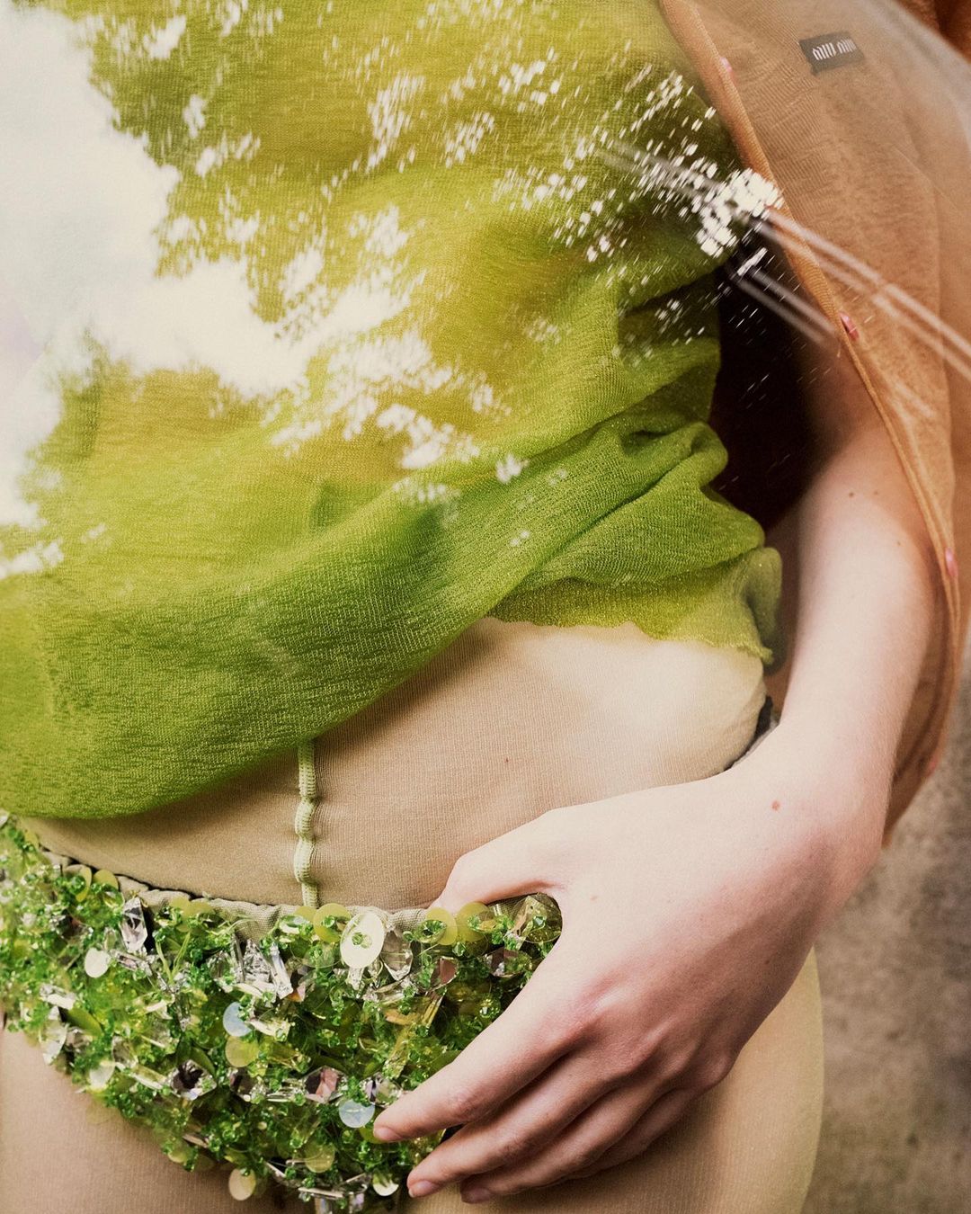 Woman in beaded belt and sheer top, filtered with tree branch, cloud, and sky overlay creating an ethereal and artistic effect.