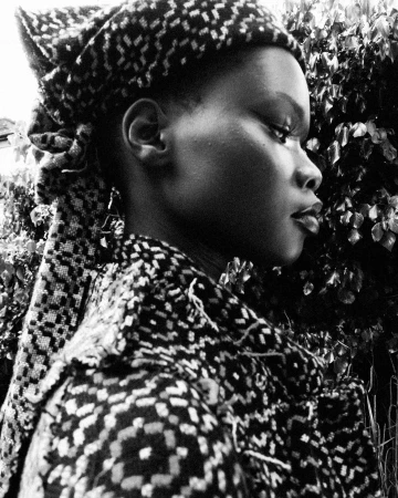 Black and white profile portrait of a woman wearing a patterned headscarf and matching coat against foliage by Chieska Fortune Smith