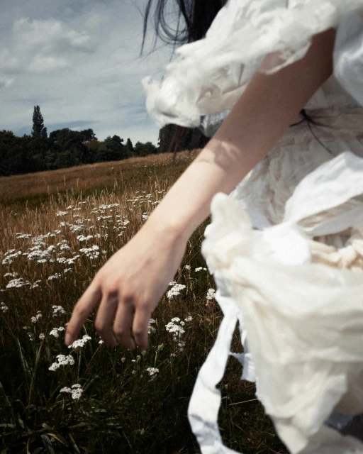 Woman in ethereal white dress walking through a field of wildflowers on a sunny day. Soft, dreamy lighting. 