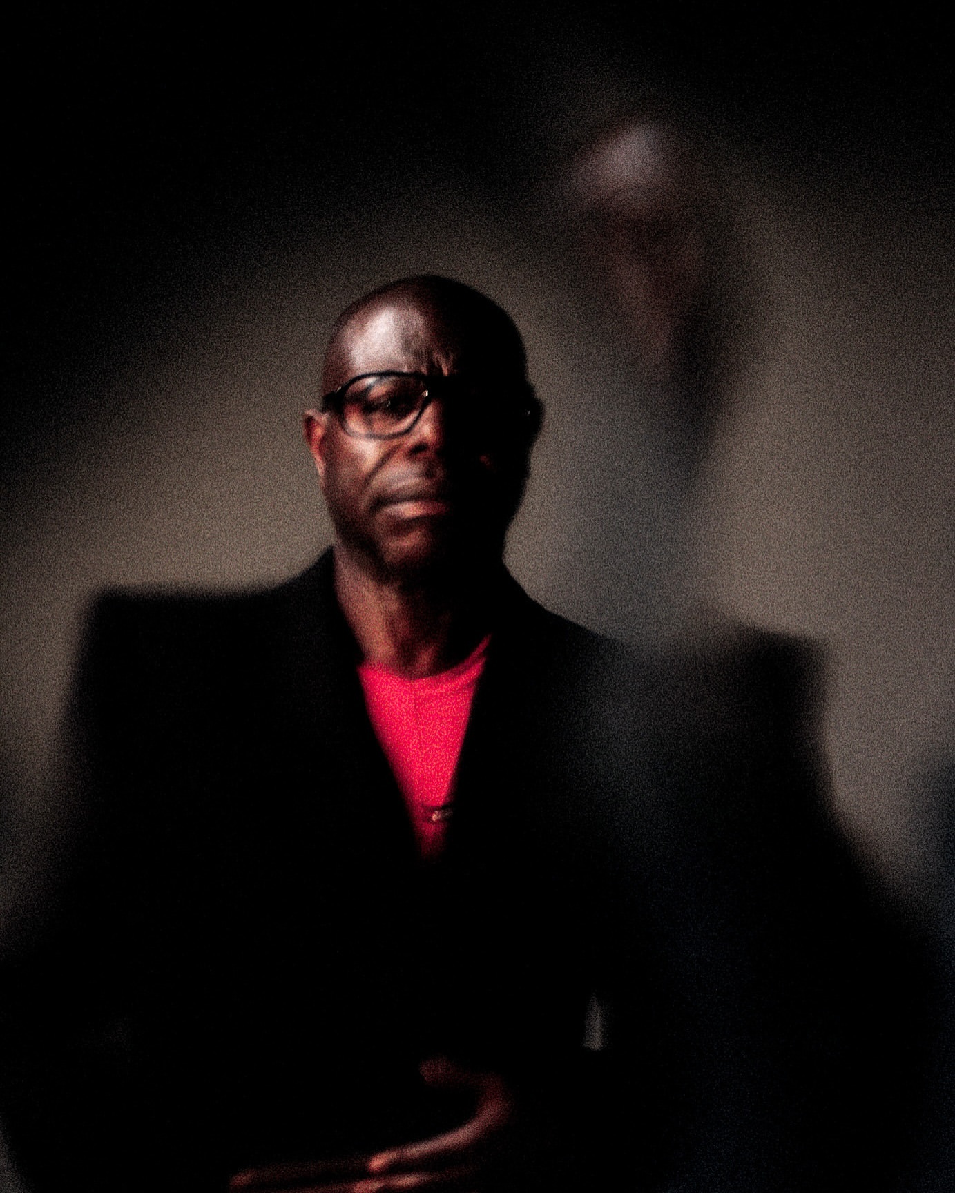 Portrait of an African-American man in a dark suit and glasses with a ghosted image of another person in the background.