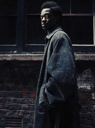 Young adult male poses in a printed overcoat in front of a brick wall and dark window, capturing urban fashion and style.