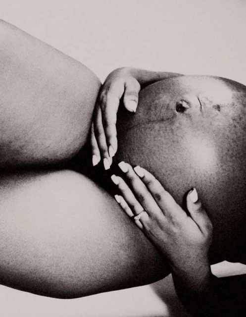 Monochrome studio shot of a pregnant adult female's abdomen, hands embracing the belly, and manicure details.