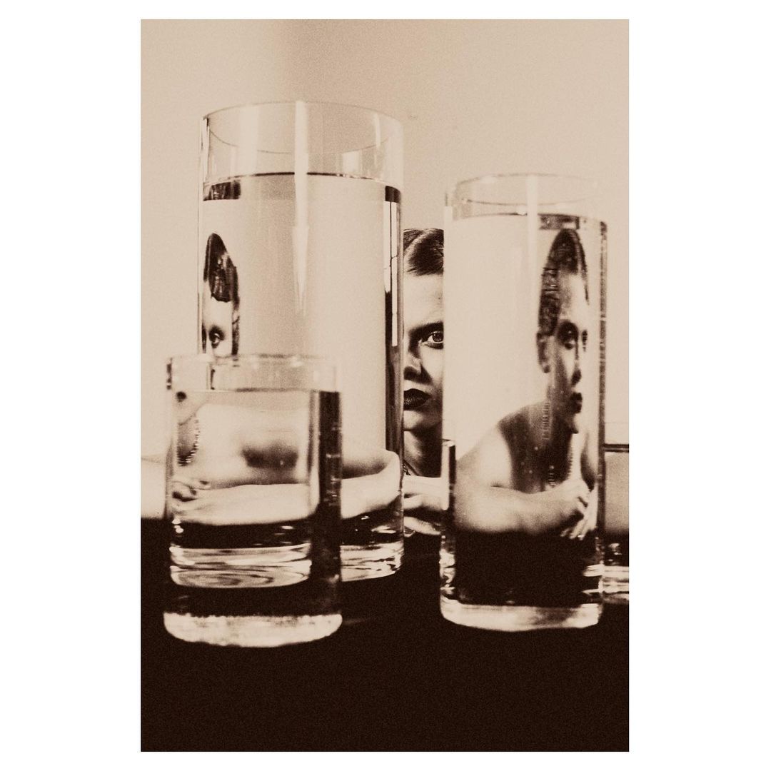 Monochrome photo of water glasses with distorted reflections of a person, creating a surreal and artistic visual statement.