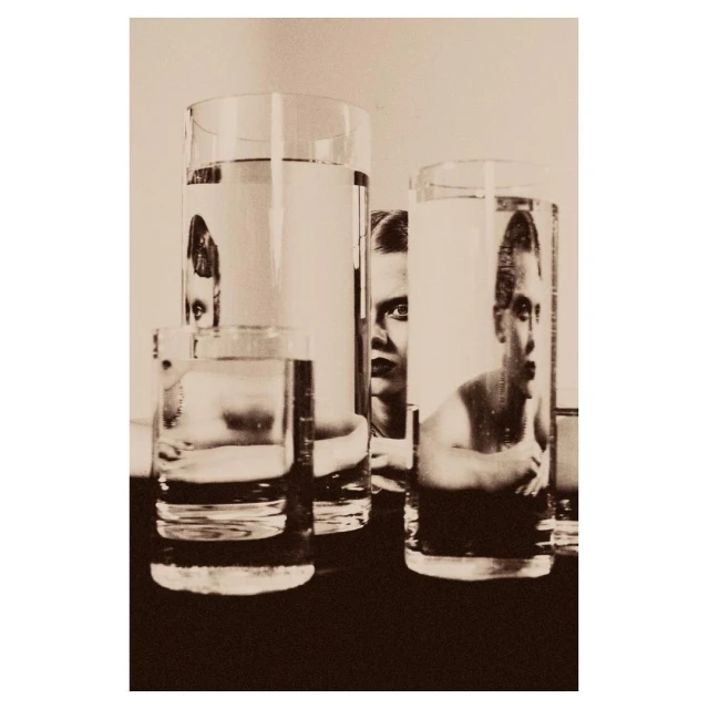 Monochrome photo of water glasses with distorted reflections of a person, creating a surreal and artistic visual statement.