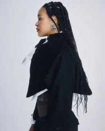 Profile portrait of a woman with braided hair wearing a black jacket and statement earring against a white background
