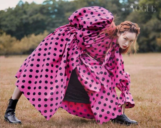 Model in voluminous pink polka dot dress and black boots bending forward on a grassy field by photographer Drew Jarrett
