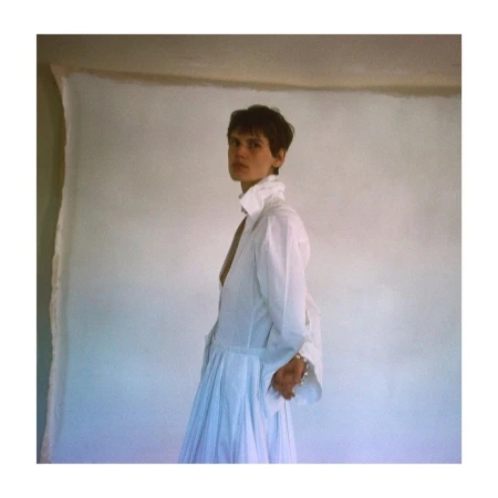 Model in a white buttoned shirt and pleated skirt standing against a textured backdrop