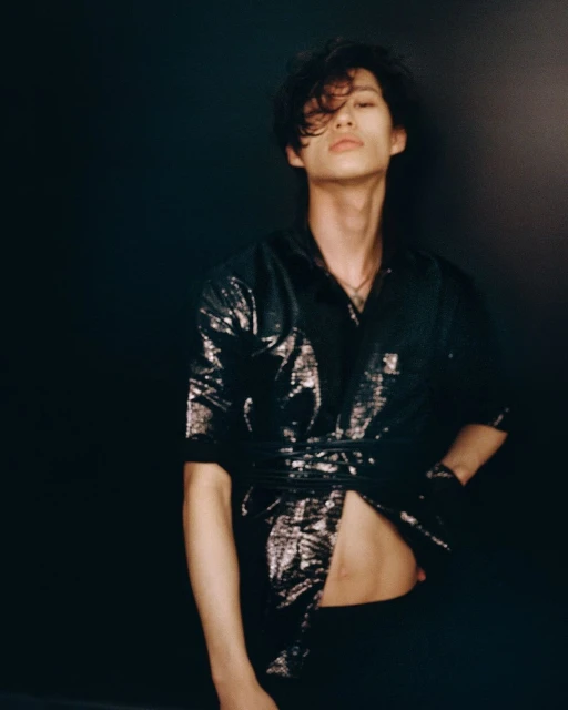 Portrait of a young adult male with dark hair wearing a sparkly shirt with a black background in a studio setting with medium framing.