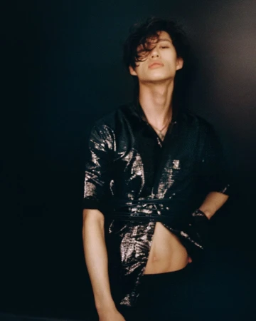 Portrait of a young adult male with dark hair wearing a sparkly shirt with a black background in a studio setting with medium framing.