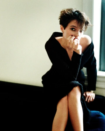 Portrait of a woman with short dark hair wearing a black off-the-shoulder dress seated indoors