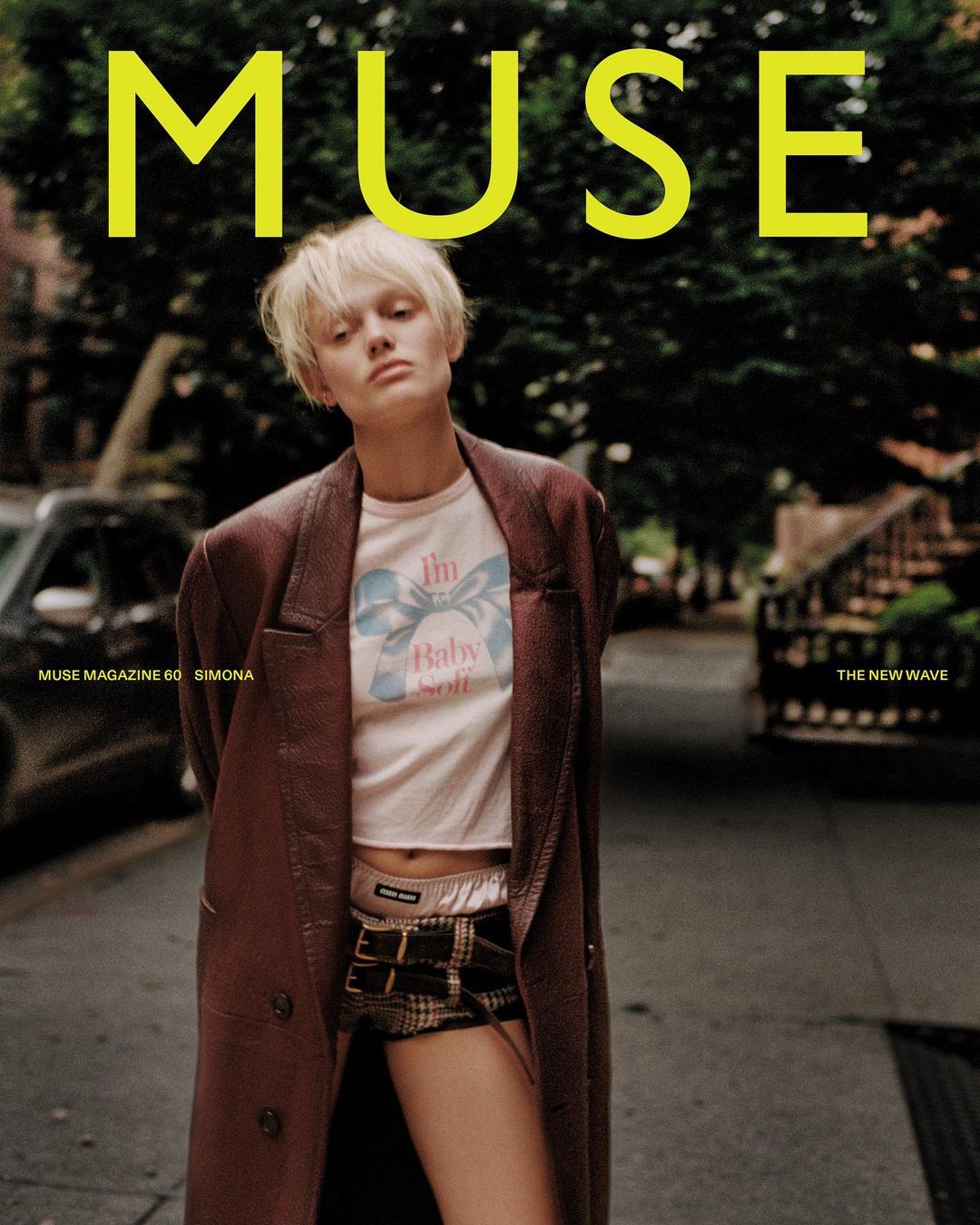 Fashion editorial cover shoot for Muse magazine features a fair-skinned woman with short blonde hair, in a long brown coat, outdoors in the city.
