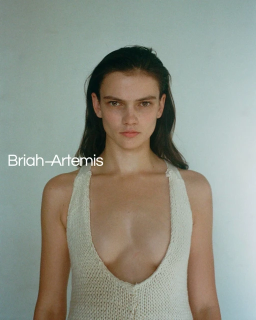 Portrait of a young adult woman with dark hair and fair skin wearing a knitted top, posing in front of a neutral background.