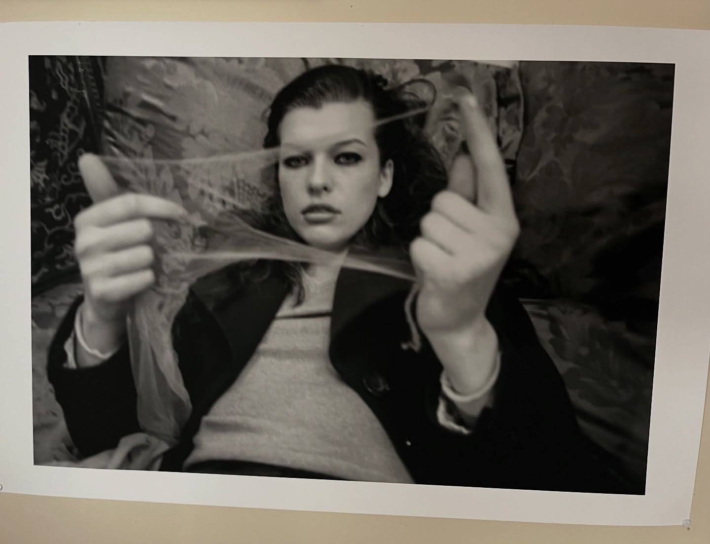 Monochrome portrait of a young woman lying down and holding a strand of string between her fingers, looking directly at the camera.