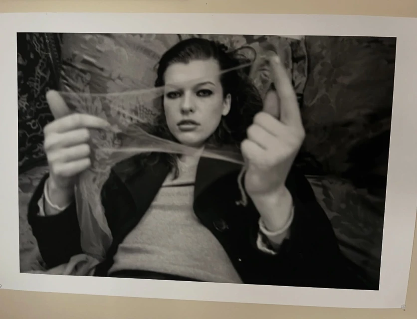 Monochrome portrait of a young woman lying down and holding a strand of string between her fingers, looking directly at the camera.