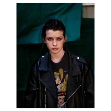 Portrait of a young woman with dark hair and a leather jacket, featuring a t-shirt with cartoon princess graphics against a green backdrop.