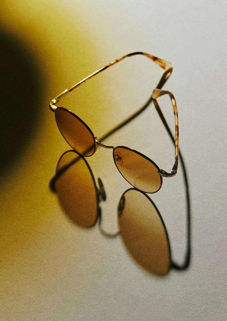 Elegant aviator-style sunglasses with brown lenses and tortoiseshell frames reflected on a glossy surface with a soft yellow glow.